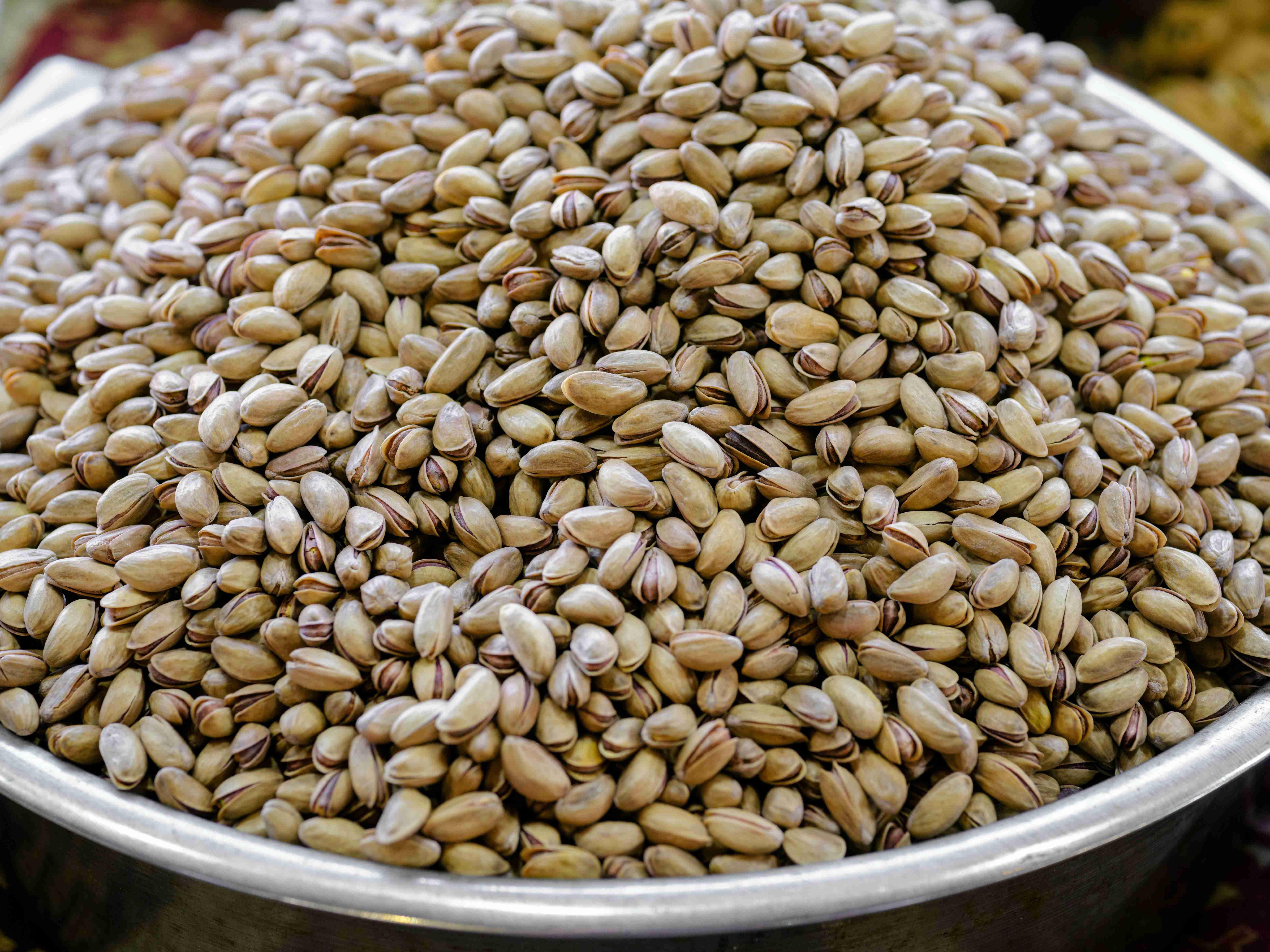 A metal bowl is pictured filled with shelled pistachios at a farmers market.