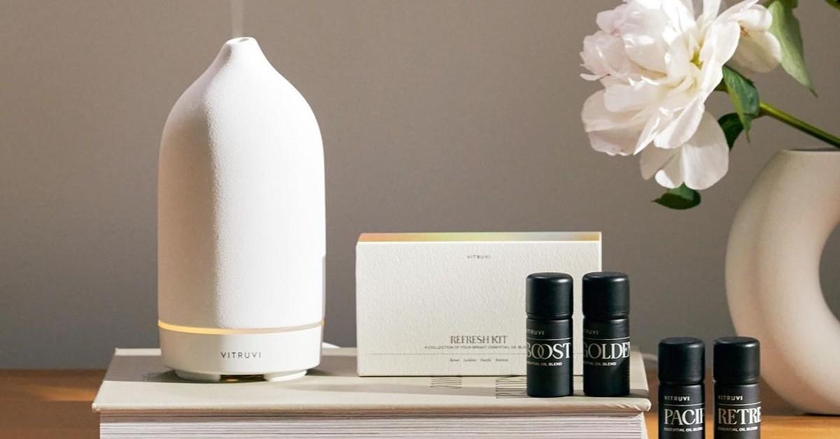 Photo of a Vitruvi oil diffuser sitting on a book beside small black bottles of various Vitruvi essential oils