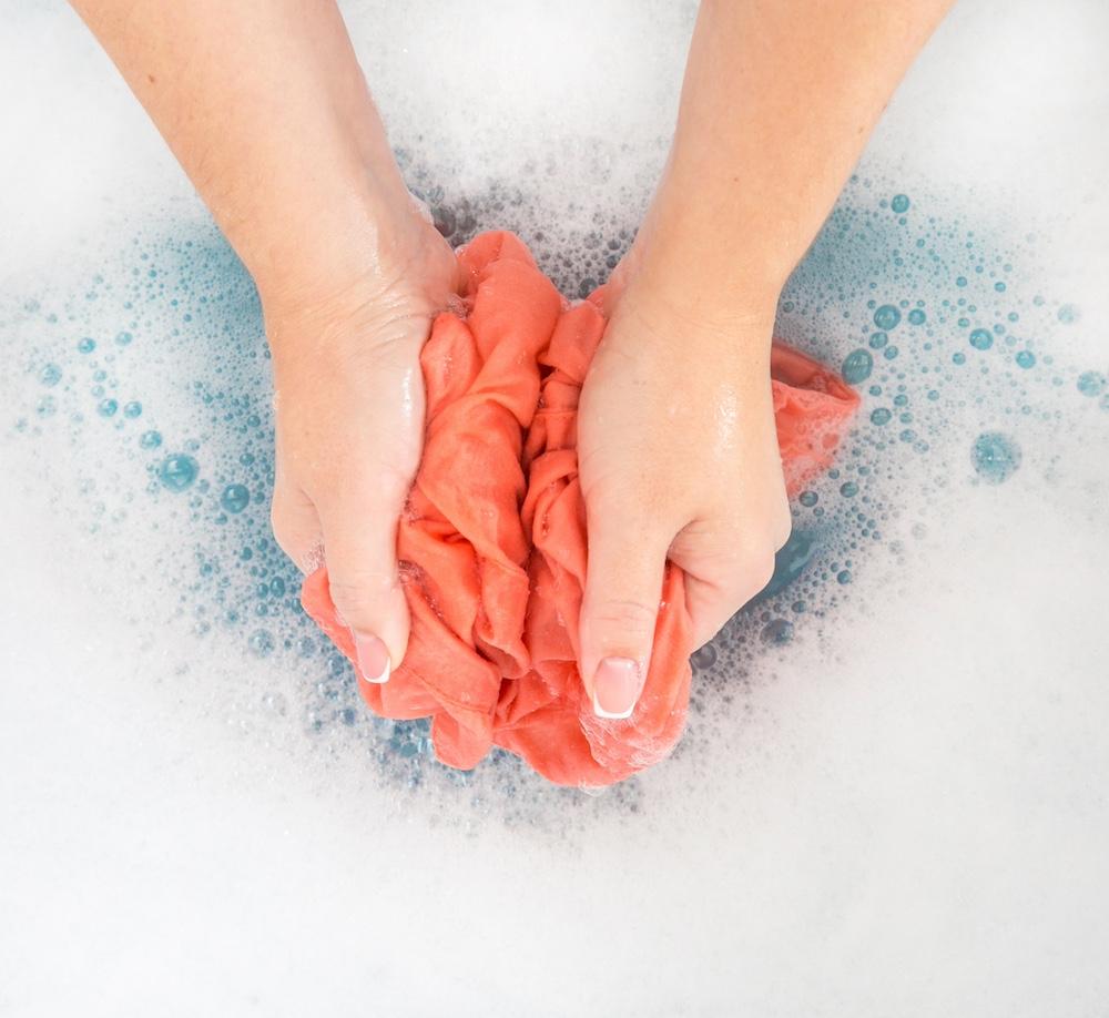Someone handwashing a piece of fabric in soapy water.