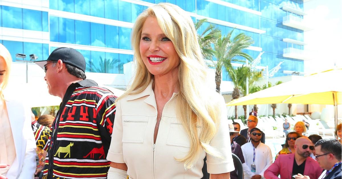 Christie Brinkley smiles while wearing a white top and red lipstick