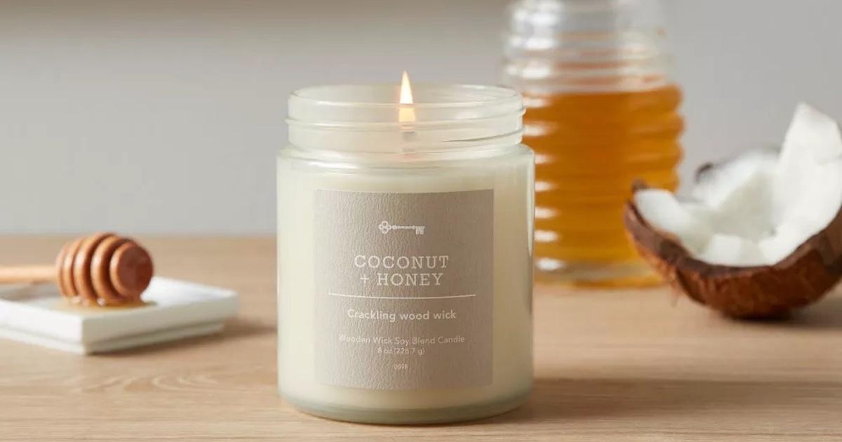 A Coconut and Honey handle is lit on a wooden surface, with a jar of honey and a coconut in the background.
