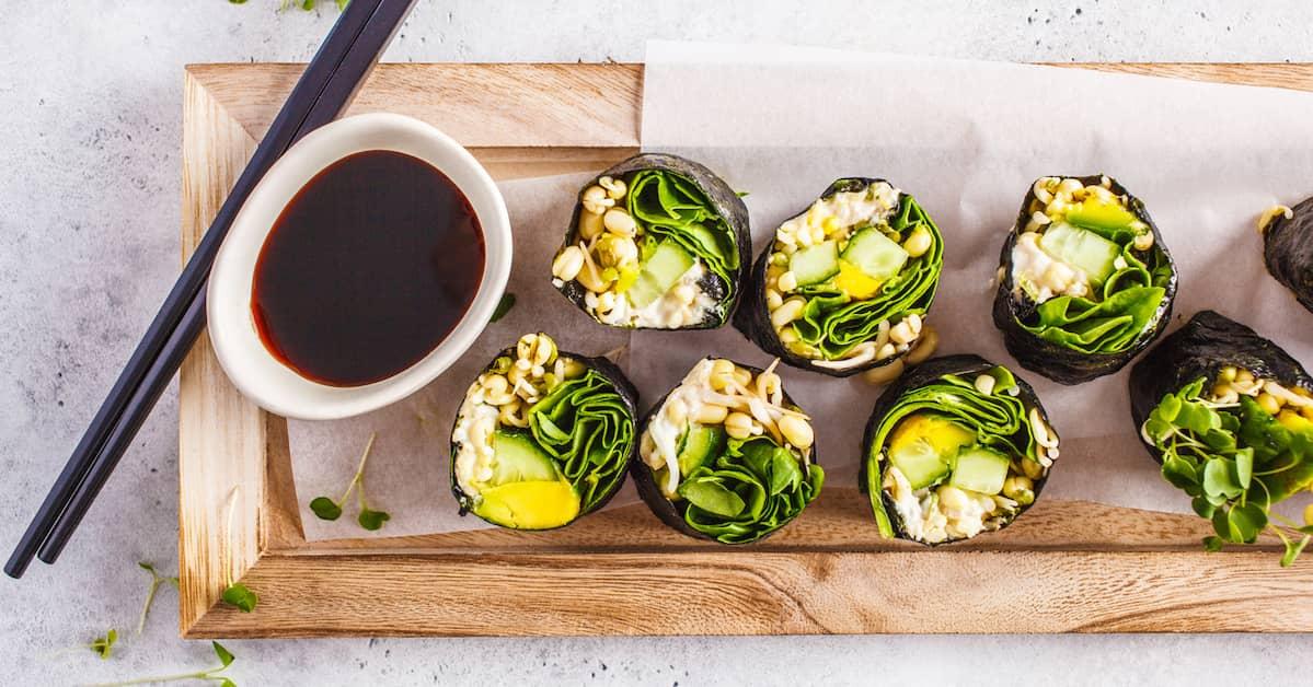 Vegan sushi, beautifully presented on a wooden plate accompanied by a bowl of soy sauce and chopsticks.