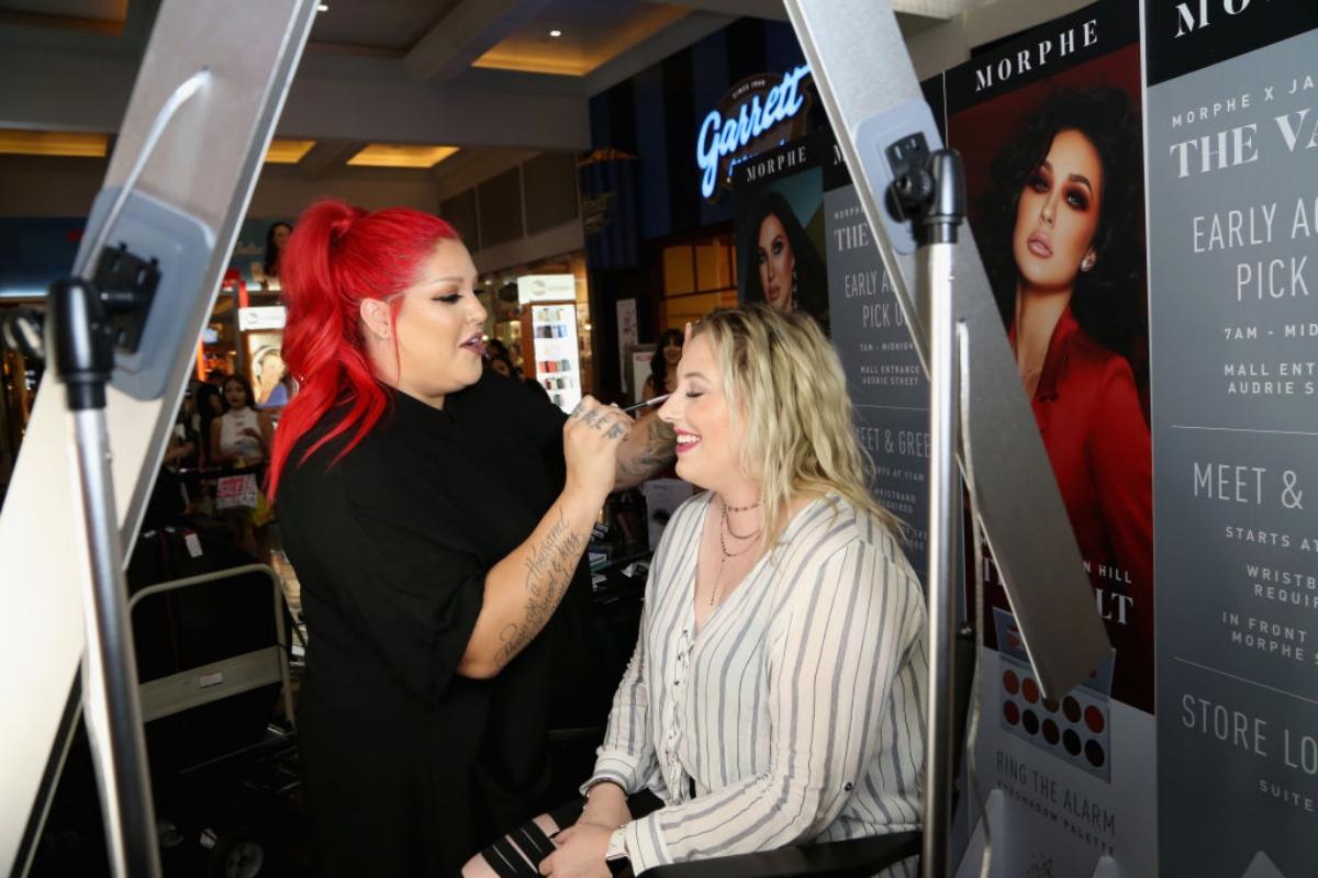 A woman with bright red hair applies makeup at a Morphe store event.
