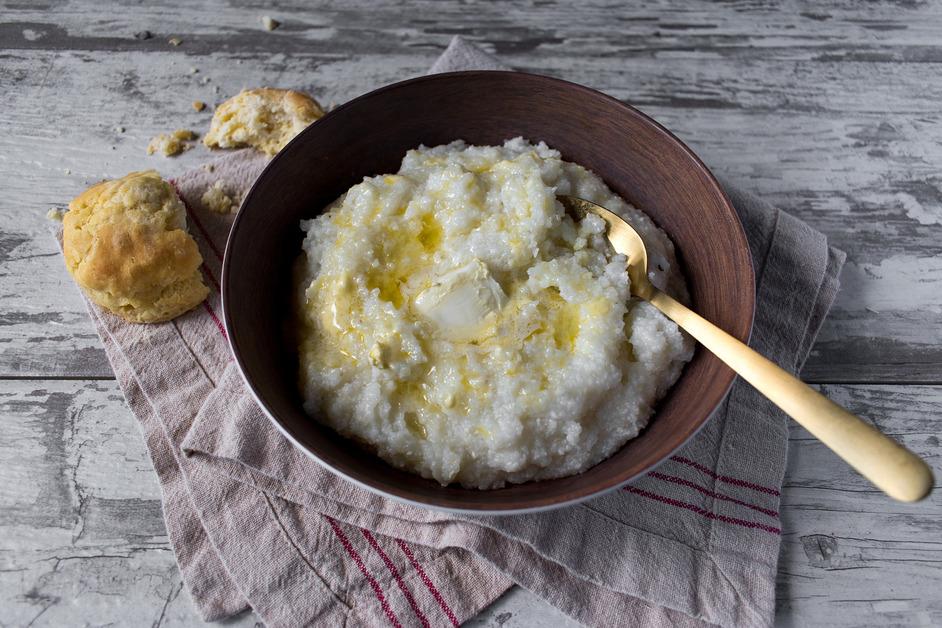 Stock photo of grits in a bowl with butter next to a biscuit.