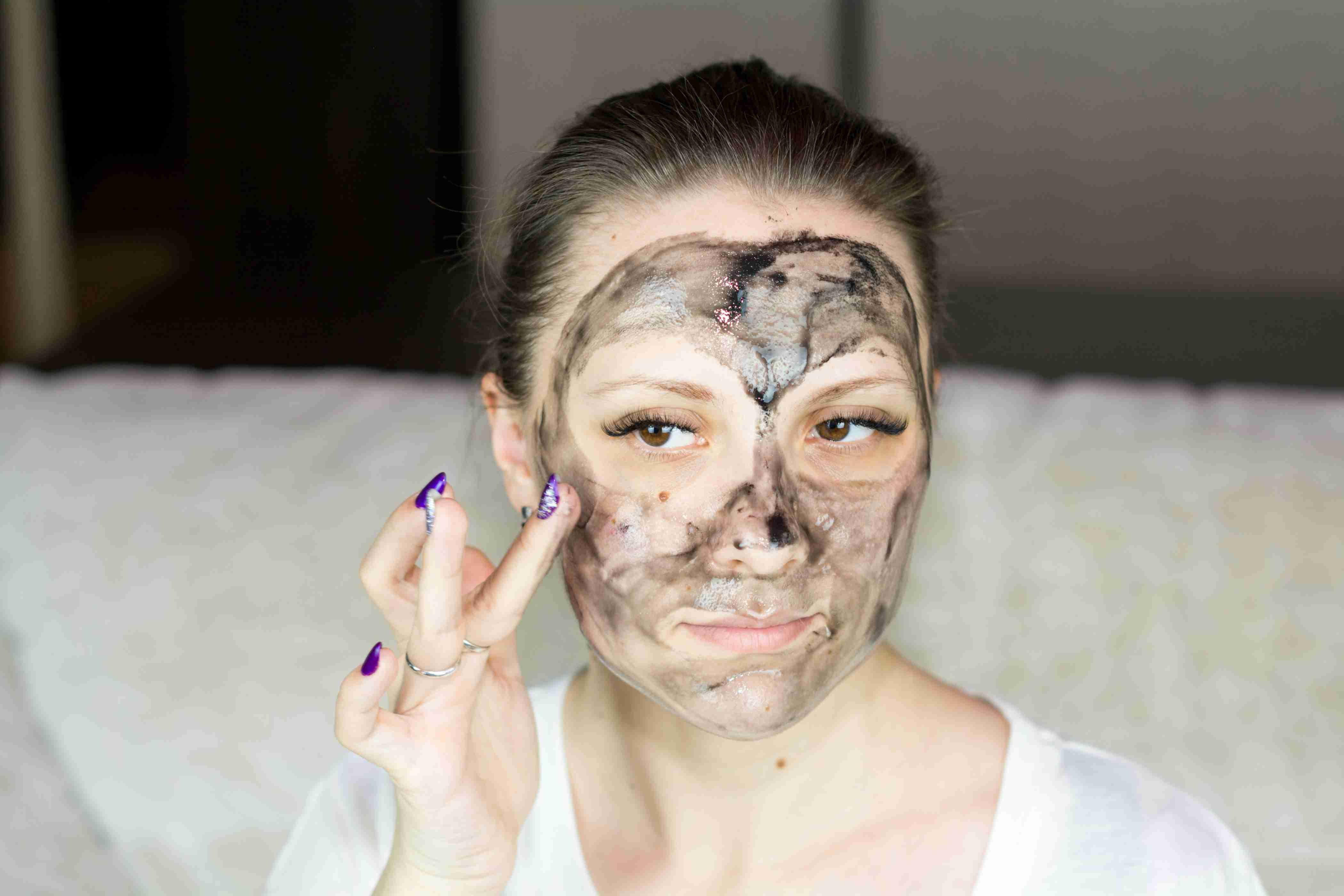 A woman uses her finger to rub a black liquid face mask onto her skin.