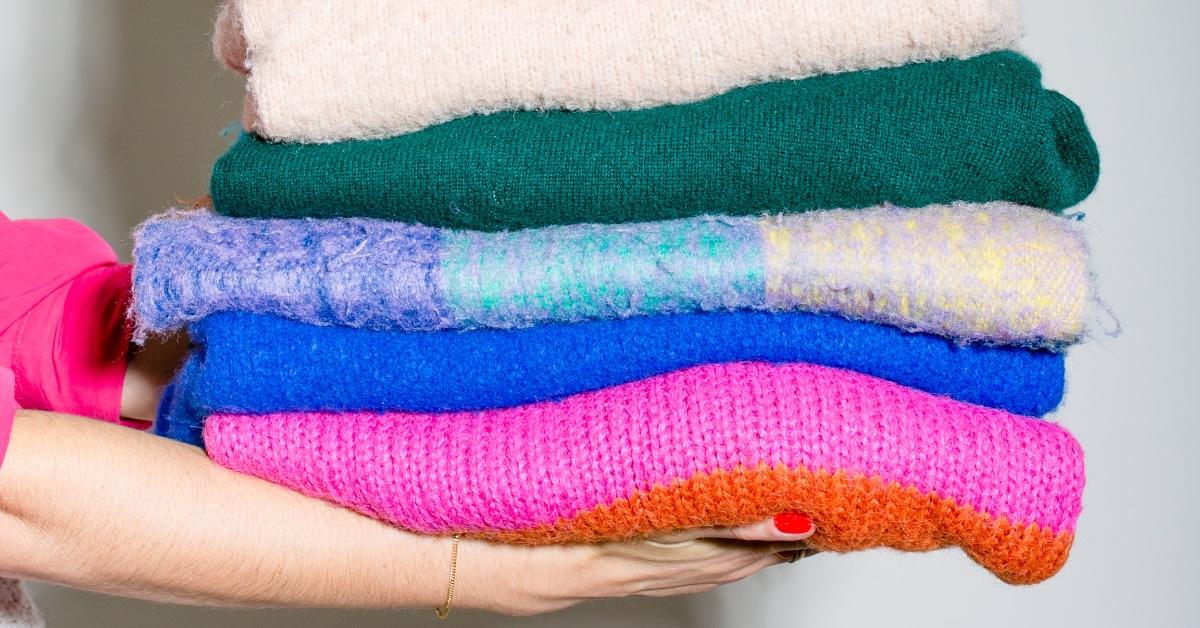Person holding folded sustainable sweaters.
